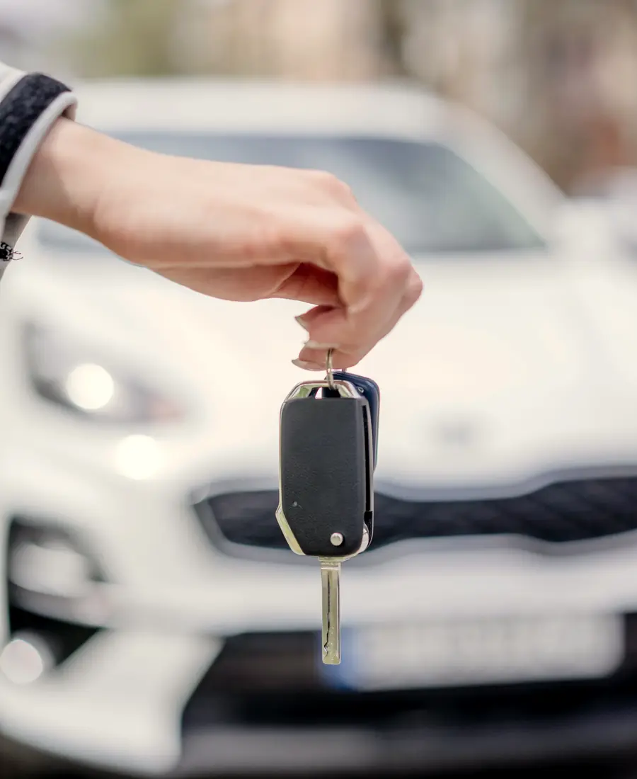 Hand holding car keys in front of a white car
