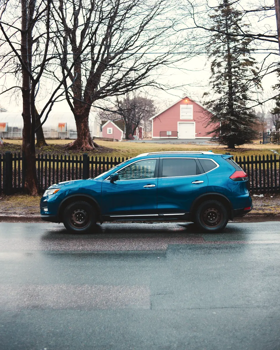 Blue Nissan Rogue parked by a red barn